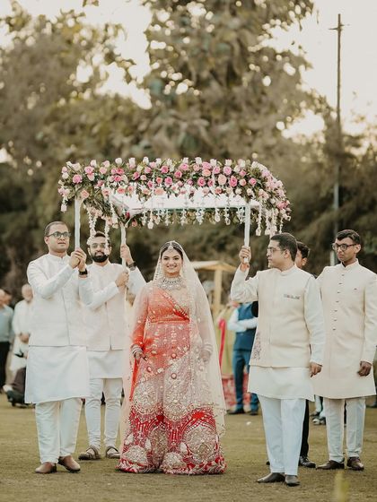 The bride's regal entrance under a phoolon ki chadar. She looks serene and graceful, a true queen walking towards her king, escorted by the most important men in her life.