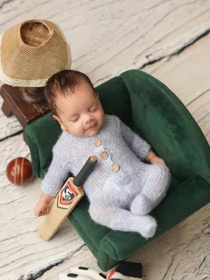 A future cricket star in the making! This newborn is posed in a miniature armchair with a tiny cricket bat and ball, a perfect theme for a cricket-loving family.