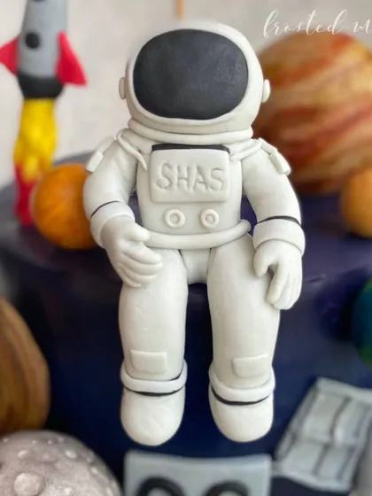 This cake is out of this world! A detailed astronaut figurine sits amongst edible planets, perfect for a space-themed celebration.