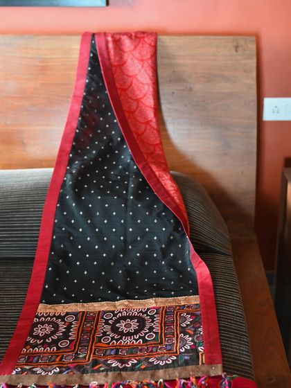 The runner draped over a headboard, showcasing its reverse side with a textured red fabric. The design is versatile and can be styled in multiple ways.