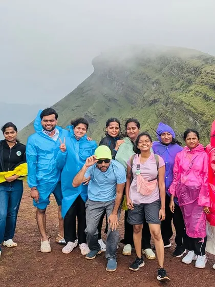 A happy group posing at the peak of the Kurinjal trek, with the unique "horse-face" shape of Kudremukha visible in the misty background.