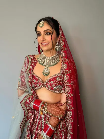 The epitome of cultural splendor. This bridal look features soft, shimmery eyes and a flawless base, perfectly complementing the traditional red and mint green lehenga.