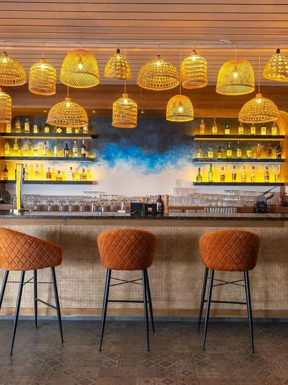 The front view of the bar at "Sloshed," where the warm glow from the cane lights illuminates the space. The design is approachable and stylish, blending natural textures with modern comfort.