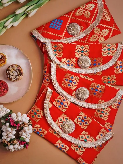 A flat lay of vibrant red and gold patterned pouches, styled with traditional Indian elements like jasmine flowers and sweets. This composition is festive and colorful, perfect for a brand specializing in ethnic accessories.