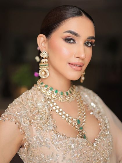 A detailed portrait showcasing the beautiful pairing of a champagne-gold lehenga with layered emerald and polki jewelry.