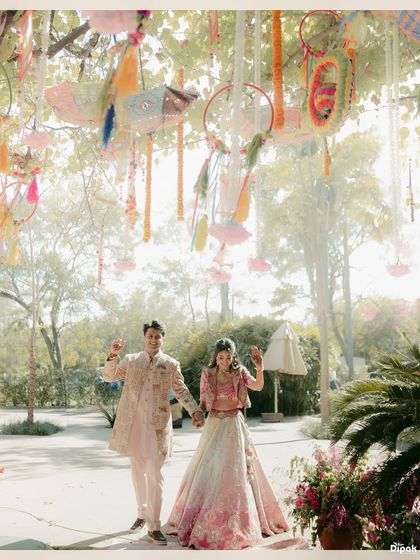 A beautiful wide shot of a couple during their Mehendi ceremony, walking hand-in-hand under a canopy of colorful decorations. This captures the festive and dreamy atmosphere.