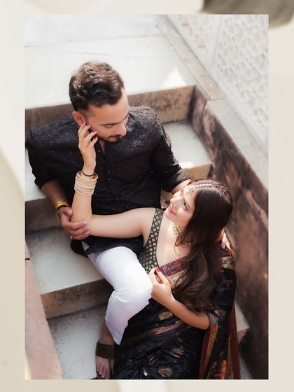 An intimate, high-angle portrait of a couple sharing a moment on a stone staircase. This candid-style shot focuses on their gentle interaction and the beautiful textures of their traditional outfits.