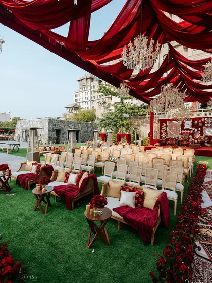 A wide-angle view of the guest seating area for the 'Laal Ishq' wedding. The setup shows the scale of the event, with lush green lawns contrasting against the rich red decor and the palace architecture.