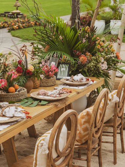 A beautifully decorated dining table on the beach, with lush, wild floral arrangements and comfortable, stylish seating.