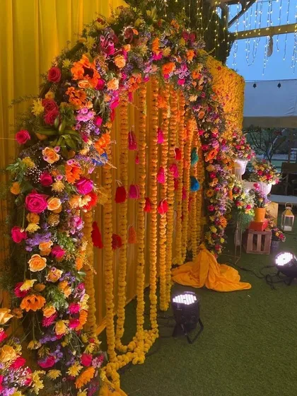 A beautiful floral archway for a Haldi ceremony, combining a traditional marigold curtain with a lush, multi-colored floral arrangement.