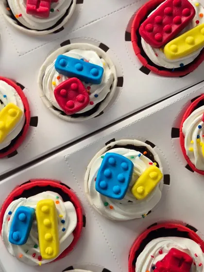 An overhead view of the LEGO-themed cupcakes. The bright, primary-colored edible blocks stand out against the white whipped cream, making them a hit with kids.