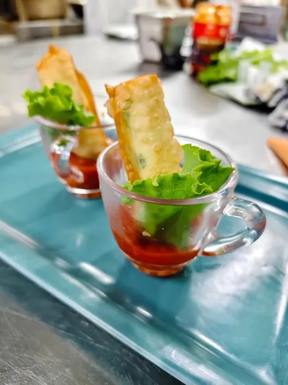 Crunch served with a side of style. These crispy spring rolls are presented in elegant glass cups with a dipping sauce, making them a chic and easy-to-eat option for any party.