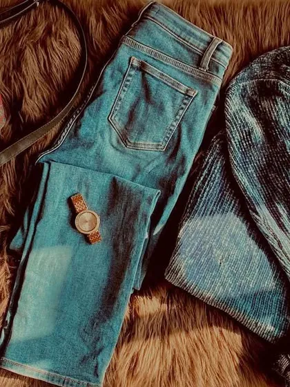 A flat lay of a cozy and stylish winter outfit. This shows how I put together a look before wearing it, combining a textured blue sweater with classic jeans, a watch, and a simple bag. Planning your outfit helps ensure all the elements work together perfectly.