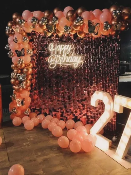 A glamorous rose gold birthday setup for a 27th birthday. The sequin wall, neon sign, and marquee numbers create the perfect backdrop for a stylish celebration.