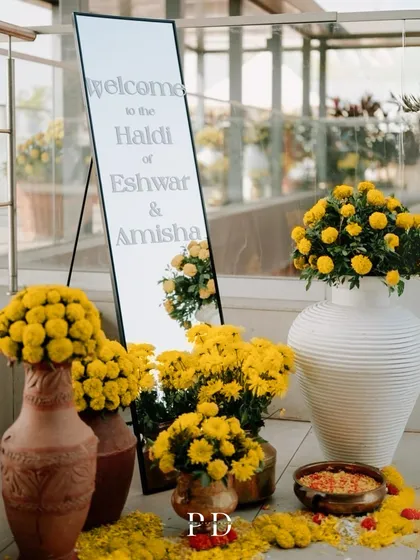 The welcome setup for a modern Haldi, featuring a sleek mirror sign and an abundance of fresh marigolds in contemporary white and terracotta vases.