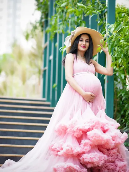 A full-length shot of a mother-to-be in a stunning pink ruffled gown, posing outdoors with a stylish hat. This is a perfect example of a high-fashion maternity look.