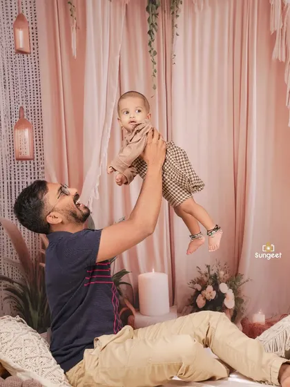 The pure joy of being lifted high by dad. This candid shot from a family milestone session captures a moment of laughter and connection, set against a soft, neutral-toned backdrop.
