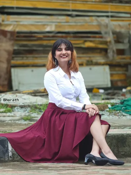 A wider shot of the model seated, showing the full flow of the maroon skirt.