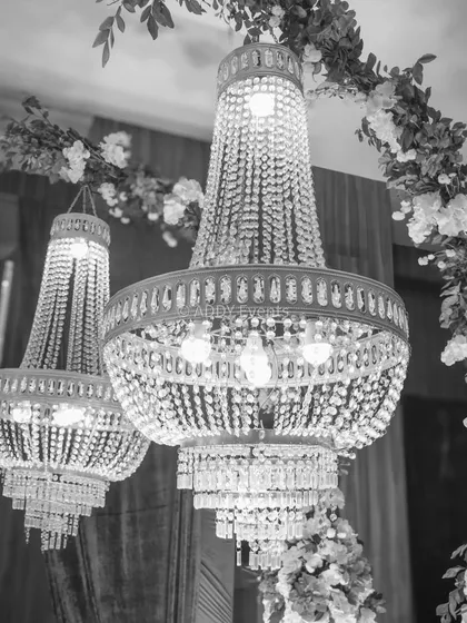 A black-and-white close-up of ornate crystal chandeliers framed by a floral arch. This artistic shot emphasizes the luxury and intricate detail we bring to our event decor.