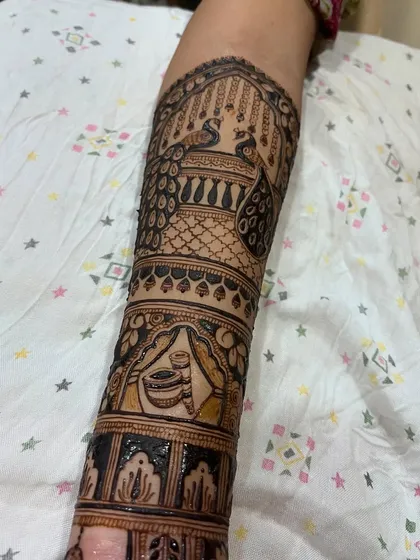 A close-up of the upper arm portion of a bridal design, showing the intricate details of peacock and kalash (pot) motifs.