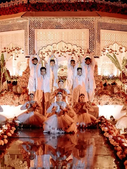 A perfectly composed varmala moment. The couple is framed by our dancers on a candle-lit, reflective stage, creating a symmetrical and visually stunning photograph that feels like a royal portrait.