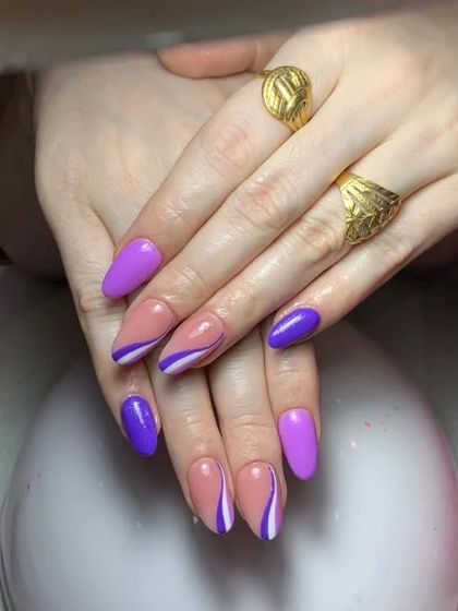 A fun and modern design with a mix of solid purple nails and abstract purple and white swirls on a nude base.