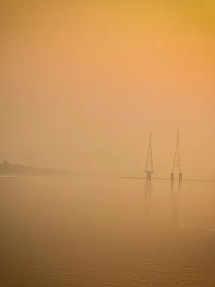 A minimalist landscape of two towers standing in calm water, enveloped in a thick, golden fog. The image is atmospheric and almost abstract in its simplicity.