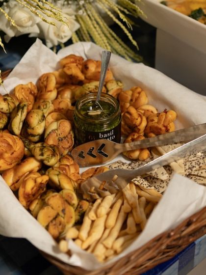 A basket of our freshly baked bread twists and grissini, served with a jar of our farm-fresh basil pesto. This is a perfect starter for any meal, showcasing our bakery and pantry offerings.