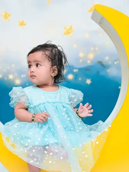 A full shot of the baby girl sitting on the yellow crescent moon against a dreamy sky. This celestial theme is a wonderful way to create magical memories of your little one.