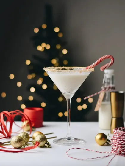 A festive vanilla cocktail in a martini glass, garnished with a candy cane. The Christmas tree bokeh and red ribbon props complete this perfect holiday drink shot.