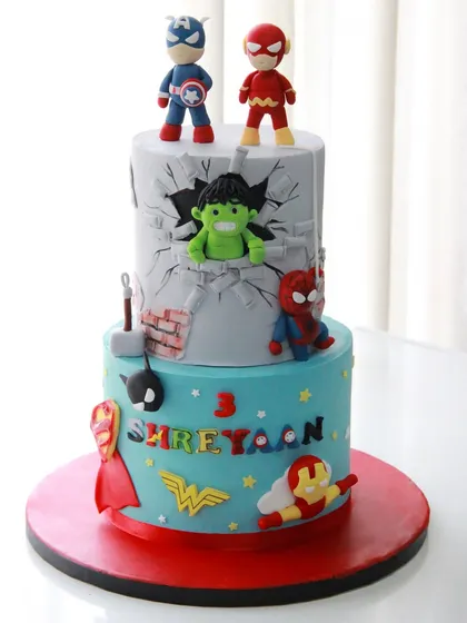 A superhero spectacular for a 3rd birthday! This two-tiered cake is packed with action, featuring the Hulk smashing through a wall, Spider-Man, Captain America, and other hero logos.