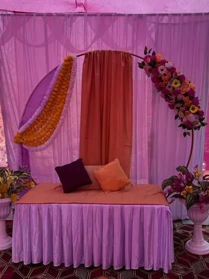 A simple and elegant seating decor for a home function. The setup uses a semi-circular arch with flowers and drapes in pastel shades.