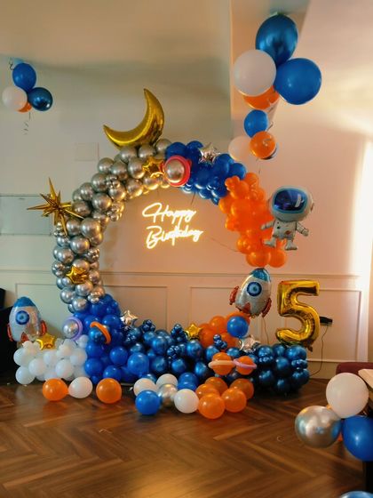 An outer space theme is always a hit. This decoration includes a silver and blue balloon arch, astronaut and rocket foil balloons, a crescent moon, and a 'Happy Birthday' neon sign.