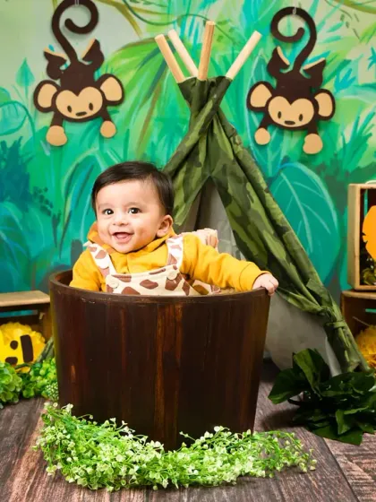 A happy baby boy enjoys his jungle-themed photoshoot, sitting in a wooden bucket surrounded by cute animal props. This shows how we can bring a creative and adventurous theme to life.