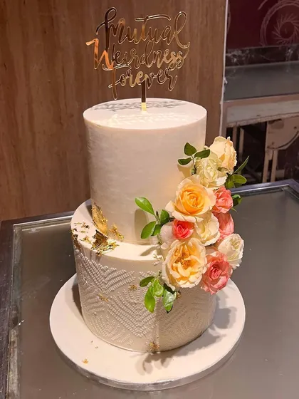 A snapshot of this two-tier beauty right before it went to the venue. The bottom tier has a modern geometric pattern, while the top is smooth, both adorned with a cascade of fresh flowers and a funny "Mutual Weirdness Forever" topper.