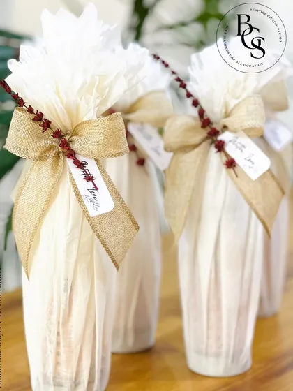 Elegant bottle wrapping for party favors or corporate gifts. Each bottle is wrapped in delicate white tissue paper and tied with a rustic burlap ribbon and a "With Love" tag for a charming, handcrafted look.