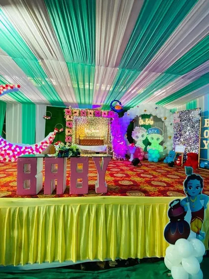A full view of a baby shower stage inside a pandal, featuring a moon prop, character cutouts, and gender reveal elements.
