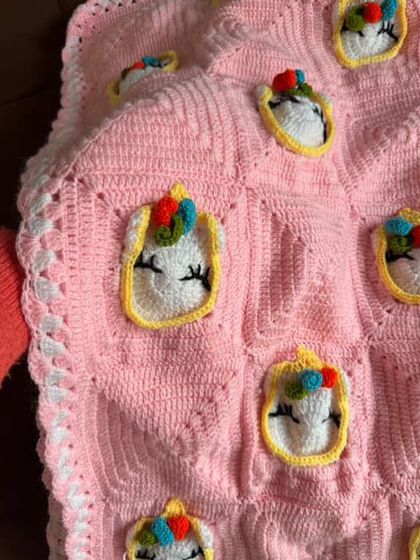 A magical unicorn-themed baby blanket in soft pink. The little unicorn faces with their colorful horns are stitched on, making it a dreamy and cozy gift.