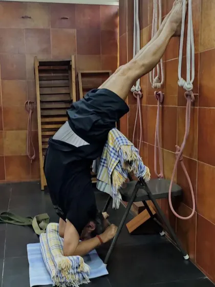 A supported headstand variation, Sirsasana, with the feet against the wall and the back supported by a chair. This builds confidence and strength for the full inversion.