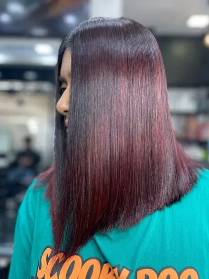 A modern, angled lob haircut featuring a blend of red and burgundy tones. The sleek, straight styling emphasizes the precision of the cut and the richness of the color.