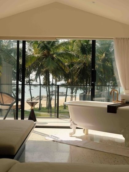 A stunning bathroom view at The Postcard Arabian Sea, where you can soak in a vintage tub while looking out at the palm trees and ocean.