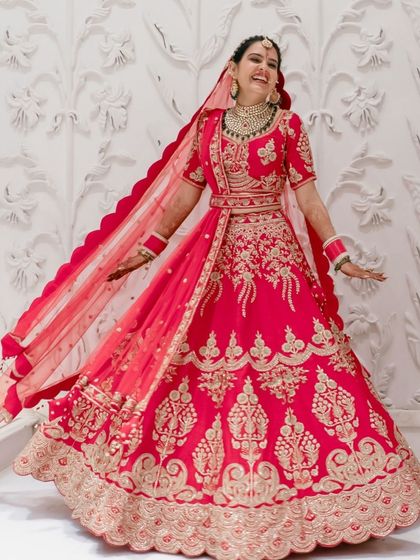 A bride's joyful twirl, showing off her magnificent pink lehenga against a clean, white architectural background.