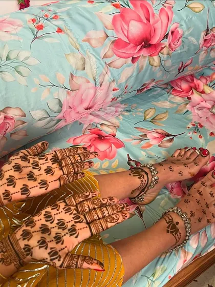 A minimal bride's complete look, with lotus buti patterns on her hands and simple, elegant designs on her feet, adorned with silver anklets.