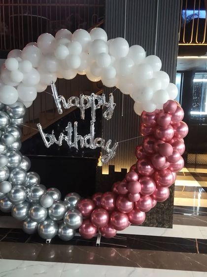 A modern birthday decoration with a three-toned balloon ring in silver, white, and metallic pink.