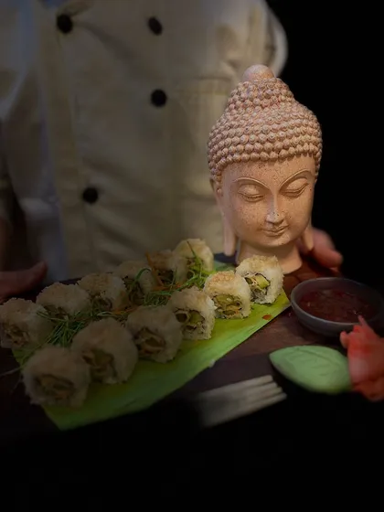 Our chef presenting a platter of our signature 'Sushi Drama'. We take pride in our presentation, using unique props like this Buddha statue to enhance the thematic feel of our Pan-Asian cuisine.
