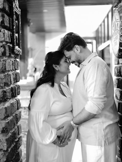 A classic and romantic black and white portrait. The couple touches foreheads in a rustic brick hallway, a moment of pure connection.