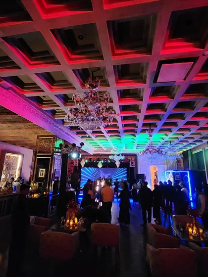 A wide view of a packed cocktail party. You can see the entire room is engaged, with a great lighting setup on the coffered ceiling that adds to the grand, festive atmosphere.