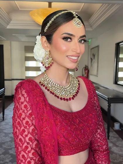 Saakshi’s crimson allure. This close-up shows her glowing skin, stunning eyes, and the beautiful floral bun that completes her bridal look.