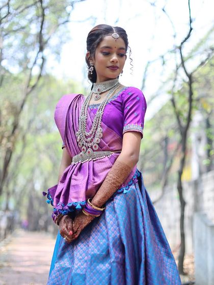 A beautiful outdoor portrait of a woman in a traditional purple and blue half saree, showcasing the elegance of the attire.