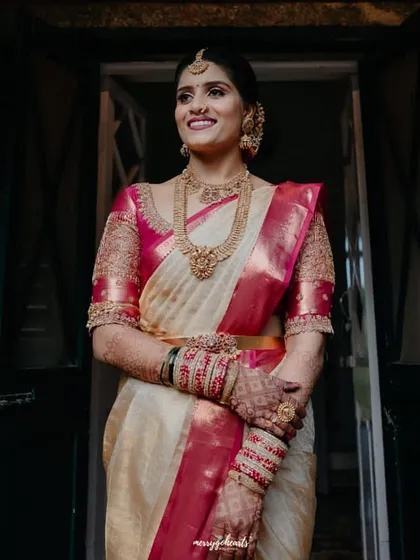 A bride in a cream and pink Kanchipuram saree. Her custom pink blouse is heavily embroidered, creating a stunning look for her muhurtham ceremony.